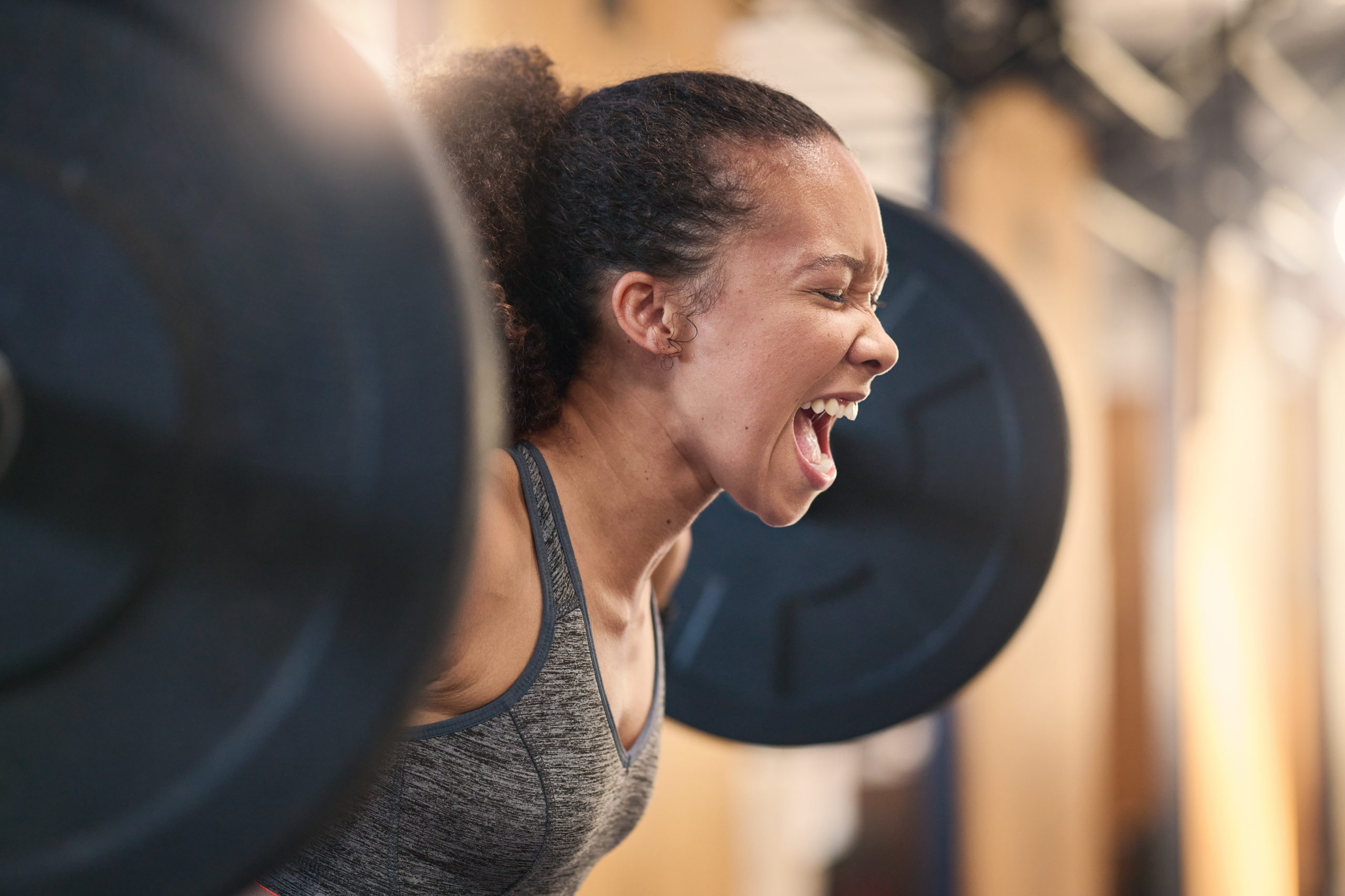 Fitness, bodybuilder and shouting with a sports black woman weightlifting in a gym for a strong bod.