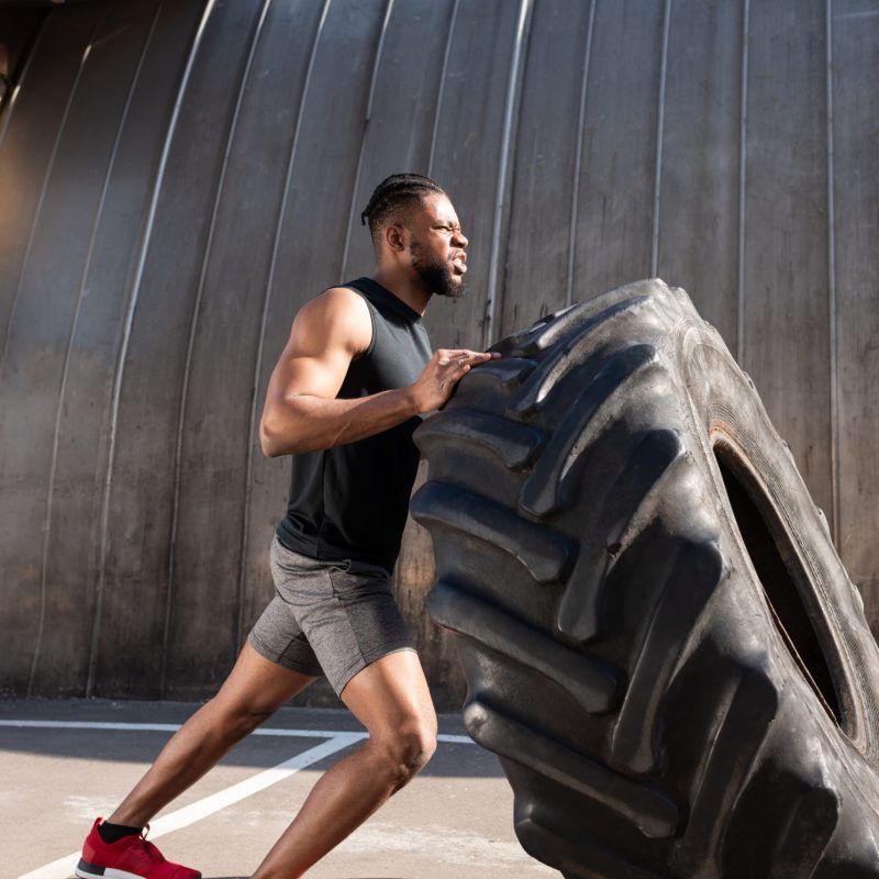athletic african american man exercising with tire on street