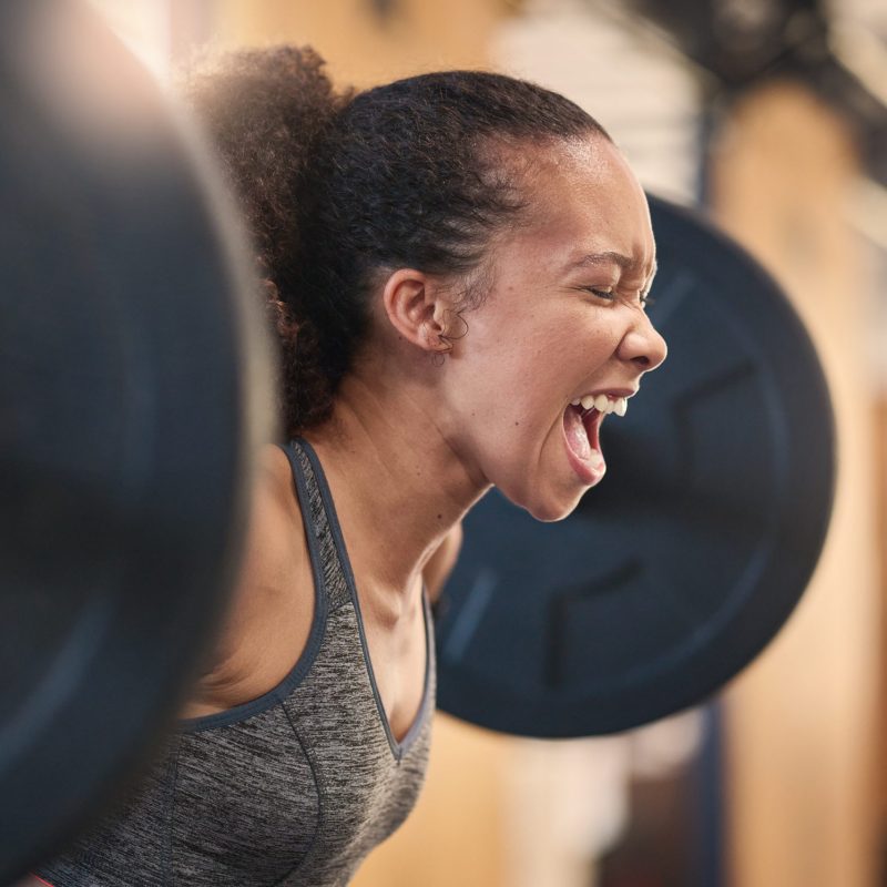 Fitness, bodybuilder and shouting with a sports black woman weightlifting in a gym for a strong bod.